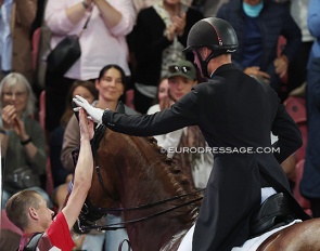 Groom Lars Seefeld high fives Daniel Bachmann Andersen who leaves the arena after his Kur to music ride on Marshall Bell at the 2022 World Championships Dressage :: Photo © Astrid Appels
