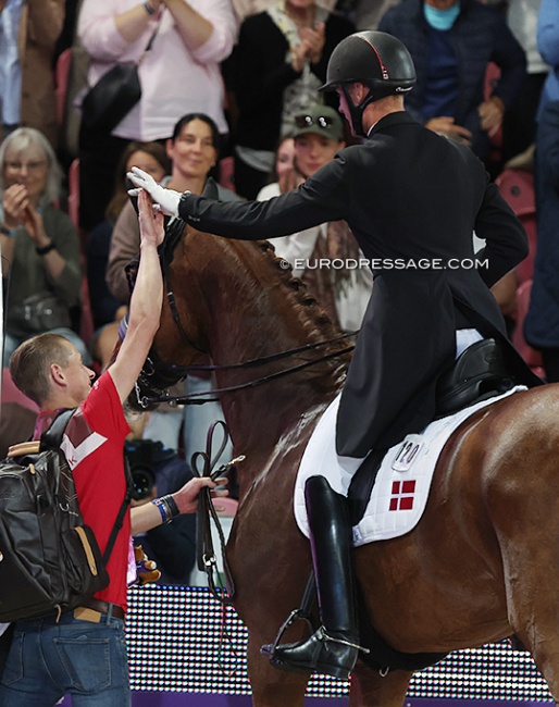 Groom Lars Seefeld high fives Daniel Bachmann Andersen who leaves the arena after his Kur to music ride on Marshall Bell at the 2022 World Championships Dressage :: Photo © Astrid Appels